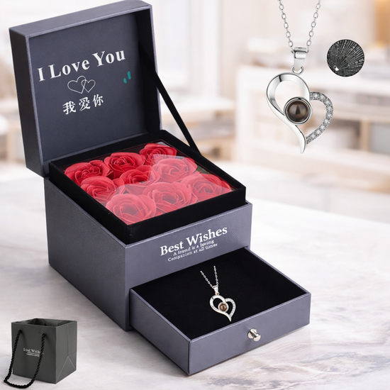 Black gift box with red roses, two heart-shaped necklaces, and a small black bag on a light wooden surface.