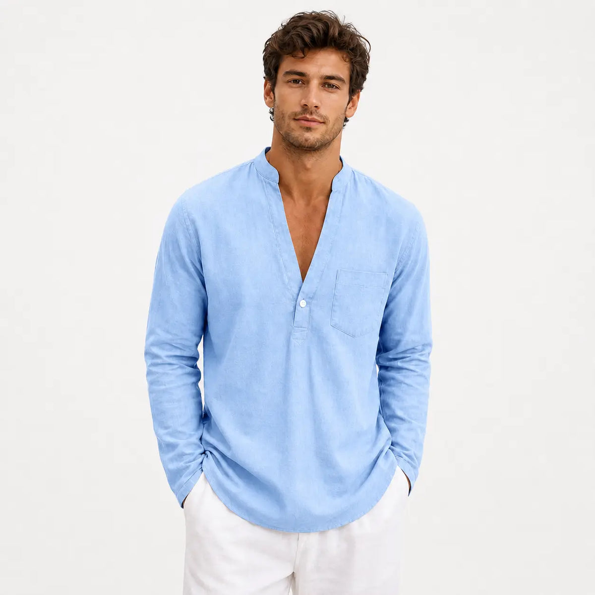 Men's linen loose fit long sleeve shirt in light blue, worn by a model with hands in pockets against white background.