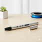 3D printing pen on a table with a spool of filament in the background
