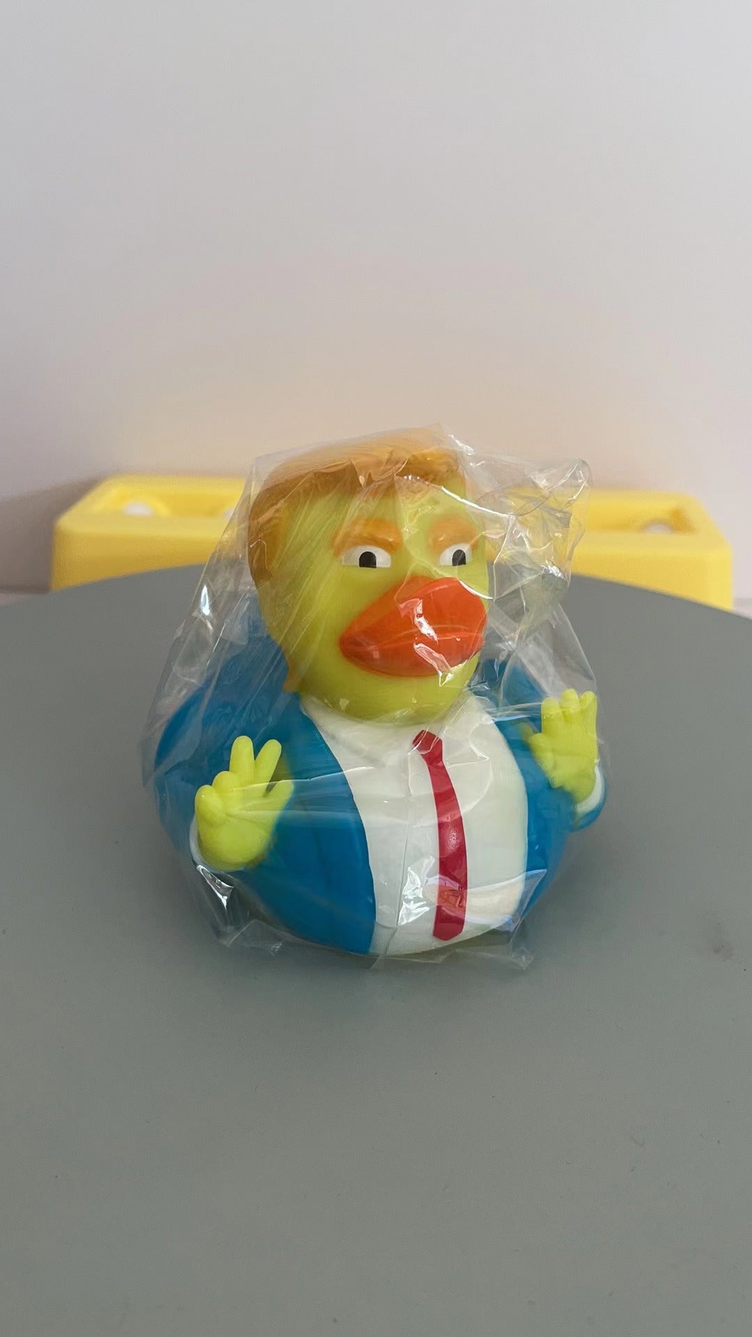 Front view of packaged duck bath toy figure with white shirt red tie and blue jacket