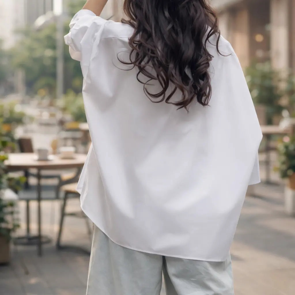 back view of a woman in a white oversized shirt paired with light gray pants outdoors