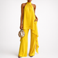 Woman wearing a yellow jumpsuit holding a gold handbag on a white background