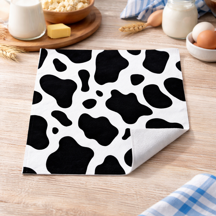 Black and white cow print towel on a wooden table with kitchen items.