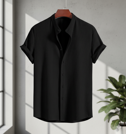 Black short-sleeve shirt on a hanger with a plant in the background