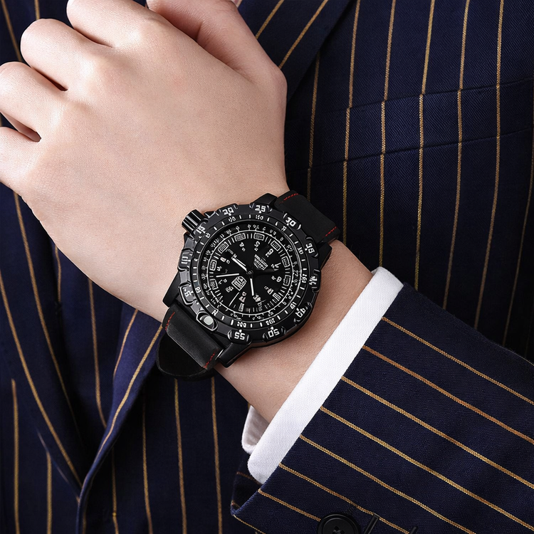 Black wristwatch on a person wearing a dark suit with gold stripes.