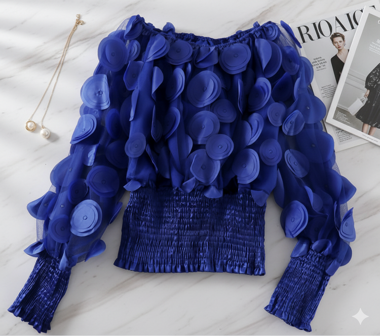 Blue floral top on a white surface with a magazine in the background