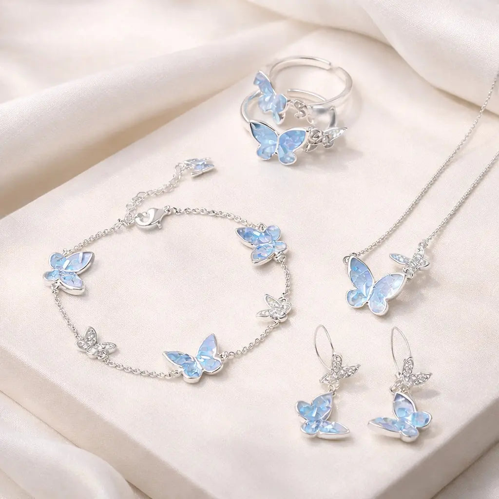 Blue crystal butterfly jewelry set for women featuring necklace, bracelet, earrings, and ring on white fabric