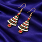 Christmas tree-shaped earrings with red berries on a blue fabric background