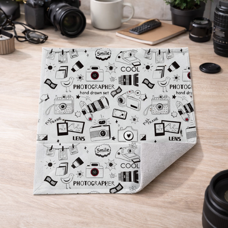 Folded blanket with black and white camera-themed pattern on a wooden surface.