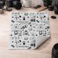 Folded blanket with black and white camera-themed pattern on a wooden surface.