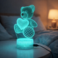 Glowing blue wireframe teddy bear lamp on a bedside table with soft lighting in the background. 3D Acrylic USB LED Night Lamp – Neon Sign
