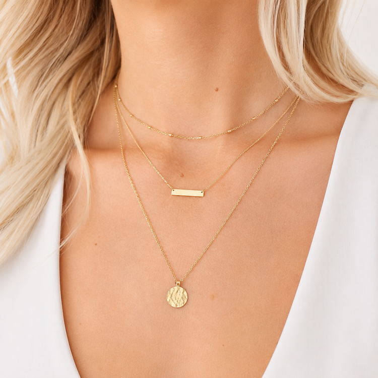 Close-up of a person wearing two gold necklaces with a plain background