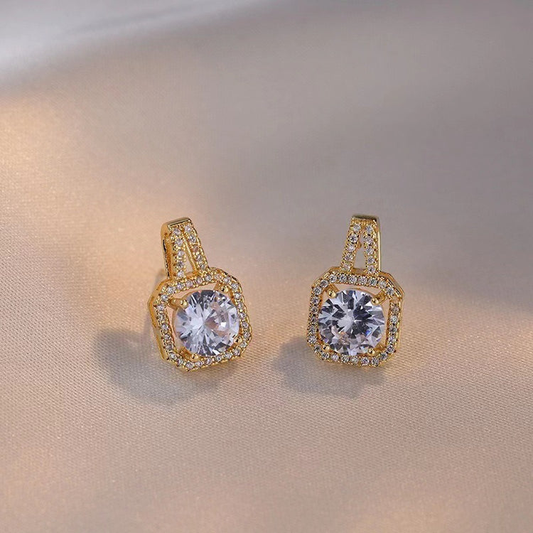 Gold earrings with clear gemstones on a beige background