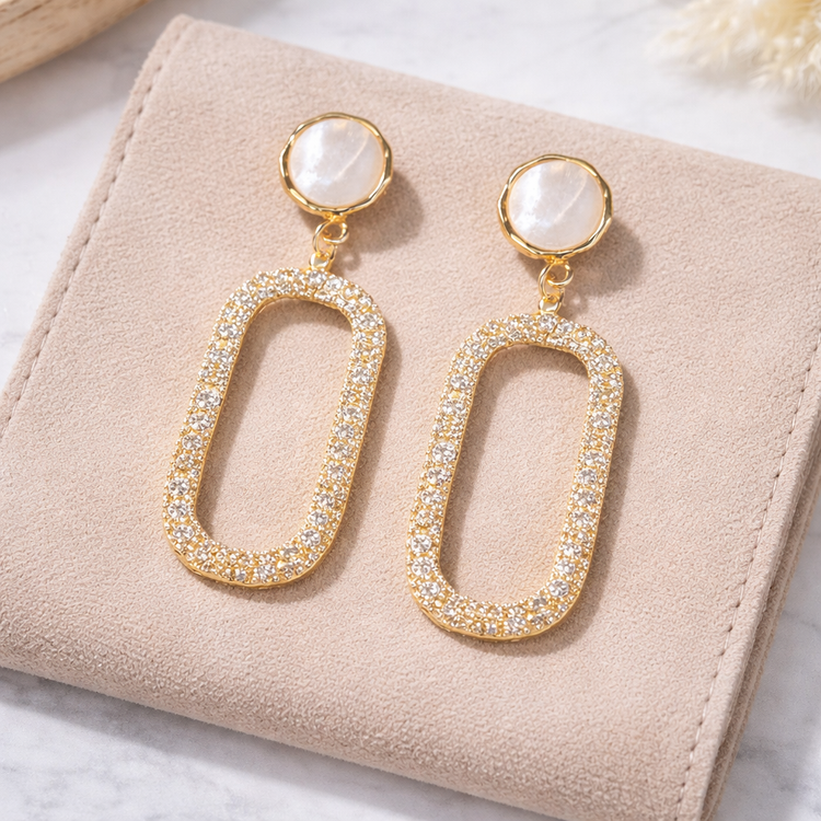 Gold earrings with oval designs and gemstones on a beige surface