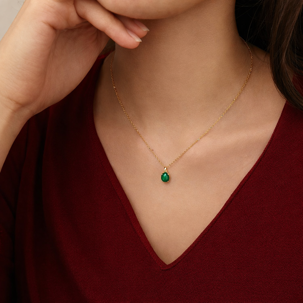 Gold necklace with a green gemstone pendant worn by a person in a red top.