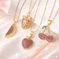 Gold necklaces with fruit-shaped pendants on a soft pink background