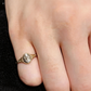 Gold ring with intricate design on a finger against a neutral background