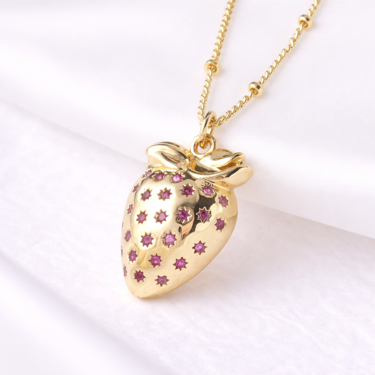 Gold strawberry-shaped pendant necklace with pink gemstones on a white background
