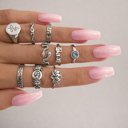 Hand wearing multiple silver rings with pink nail polish on a neutral background