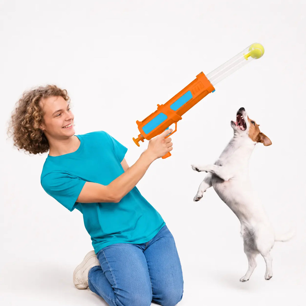 handheld dog ball launcher orange and blue plastic device held by person kneeling beside jumping dog