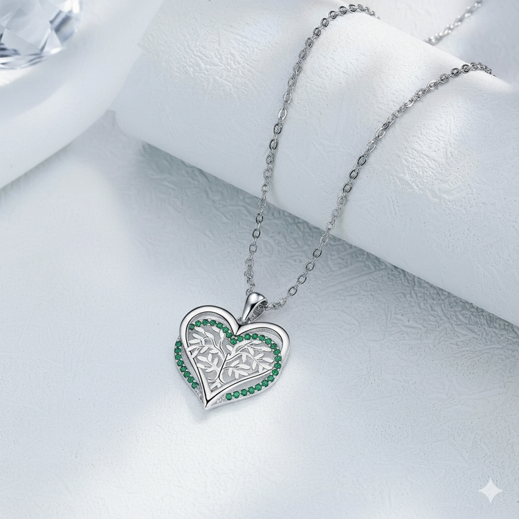 Heart-shaped silver pendant with green stones on a white surface