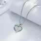 Heart-shaped silver pendant with green stones on a white surface