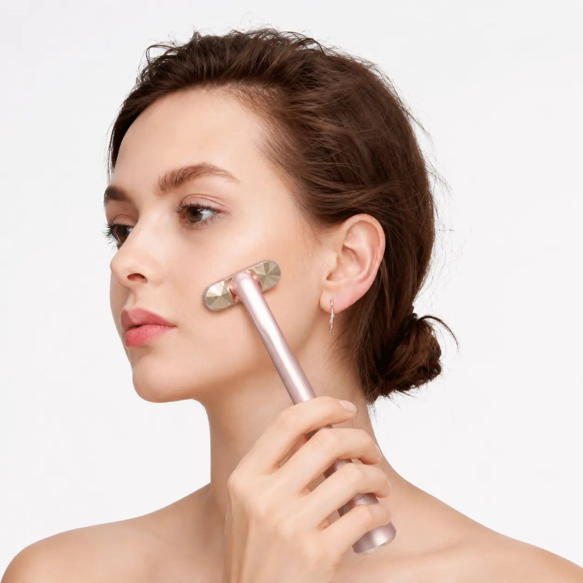 Facial massager wand for radiant skin care held by a model with brown hair in a bun against a white background