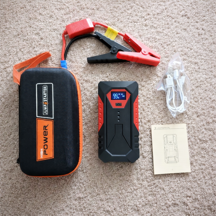 Jump starter kit with case, cables, and user manual on a carpeted floor.
