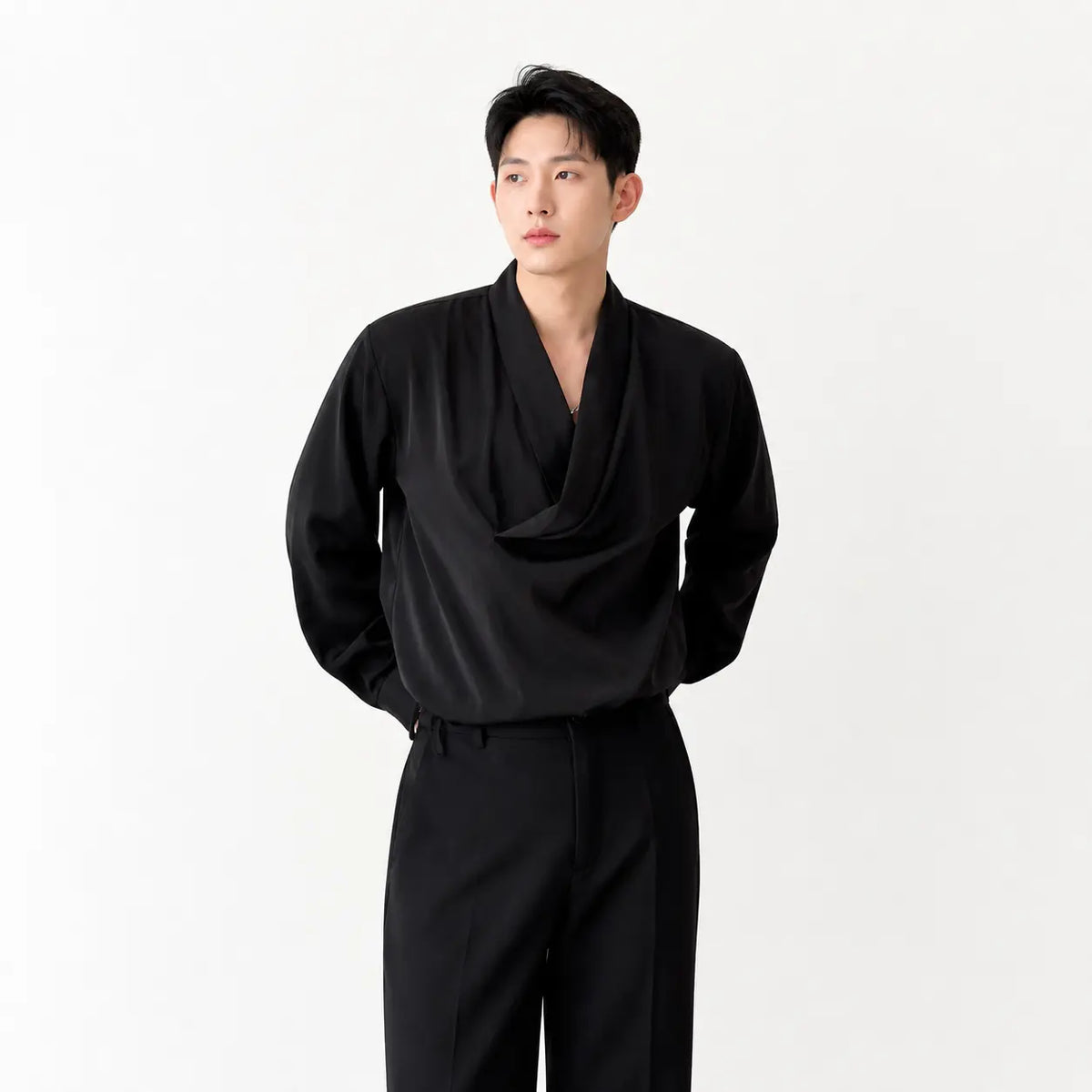 Men's loose fit silk-look shirt in black worn by a model with hands in pockets against white background