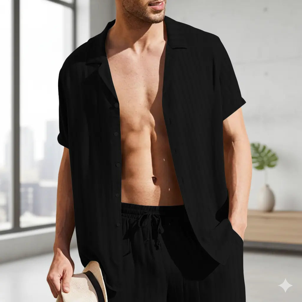 Man wearing a black open shirt and pants in a bright room with large windows.