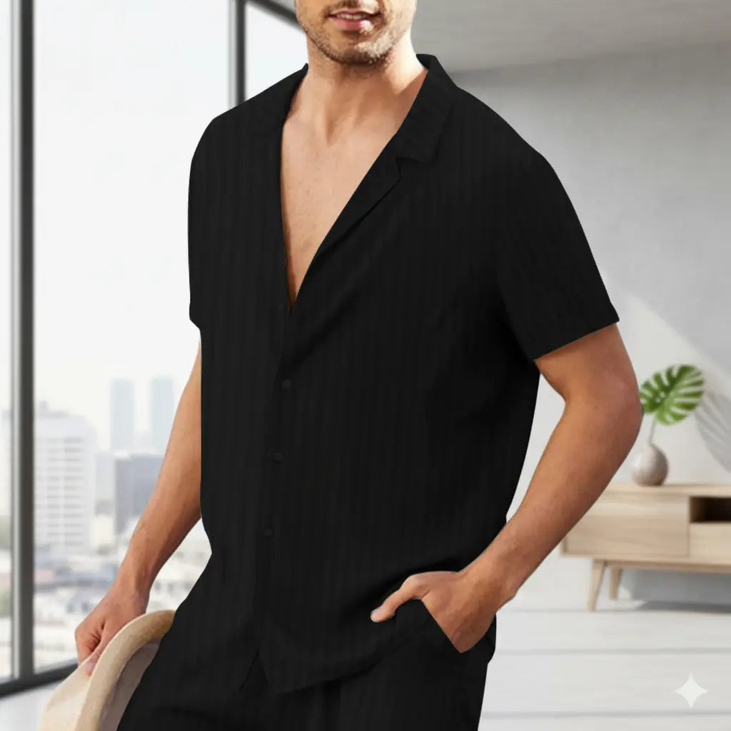man wearing a black striped short-sleeve shirt with hand in pocket standing by window