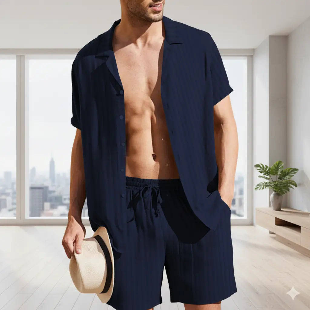 Man wearing a navy blue shirt and shorts holding a hat indoors with a cityscape view.