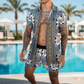 Man wearing a patterned shirt and shorts by a poolside with palm trees in the background