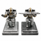 Two metallic warrior figurines on stands with one holding a pen.