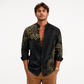 Man wearing a black shirt with gold patterns on a white background