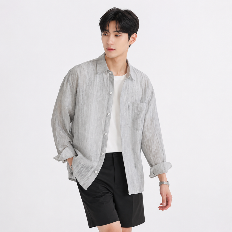 Man wearing a light gray button-up shirt over a white t-shirt with black shorts on a white background
