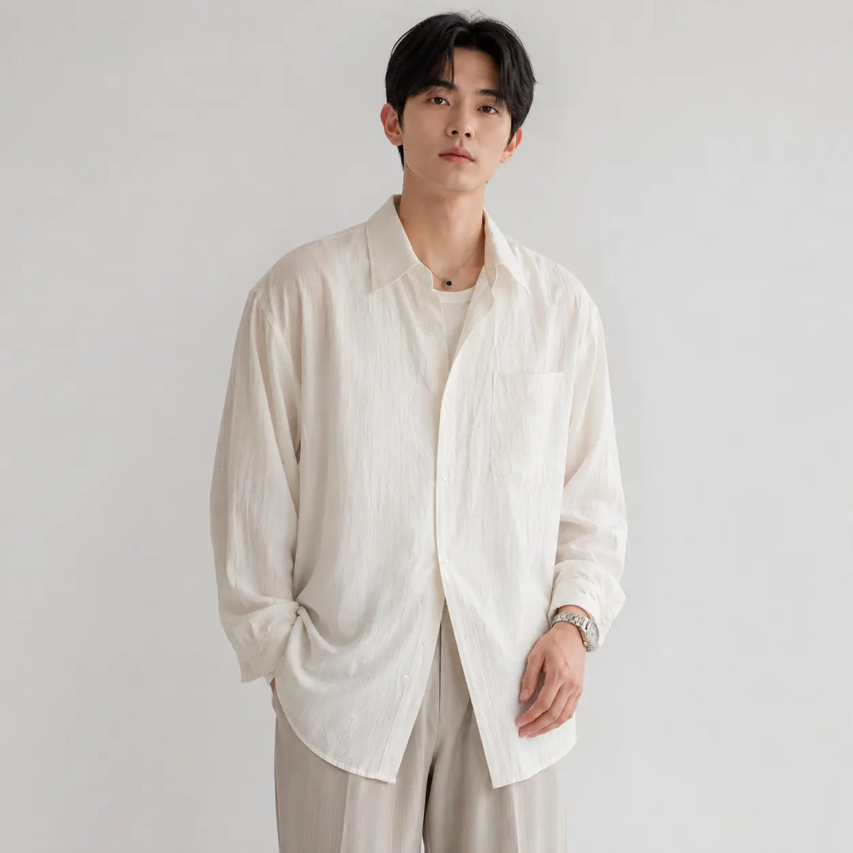 Men's linen shirt - loose fit long sleeve solid color button up in cream worn by a model with one hand in pocket.