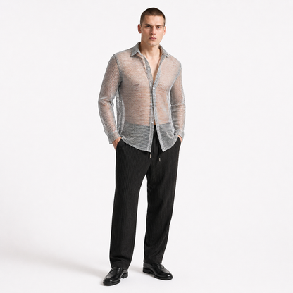 Man wearing a sheer beige shirt over a patterned shirt with black pants on a white background