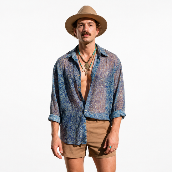 Man wearing a patterned shirt, beige shorts, and a hat on a white background