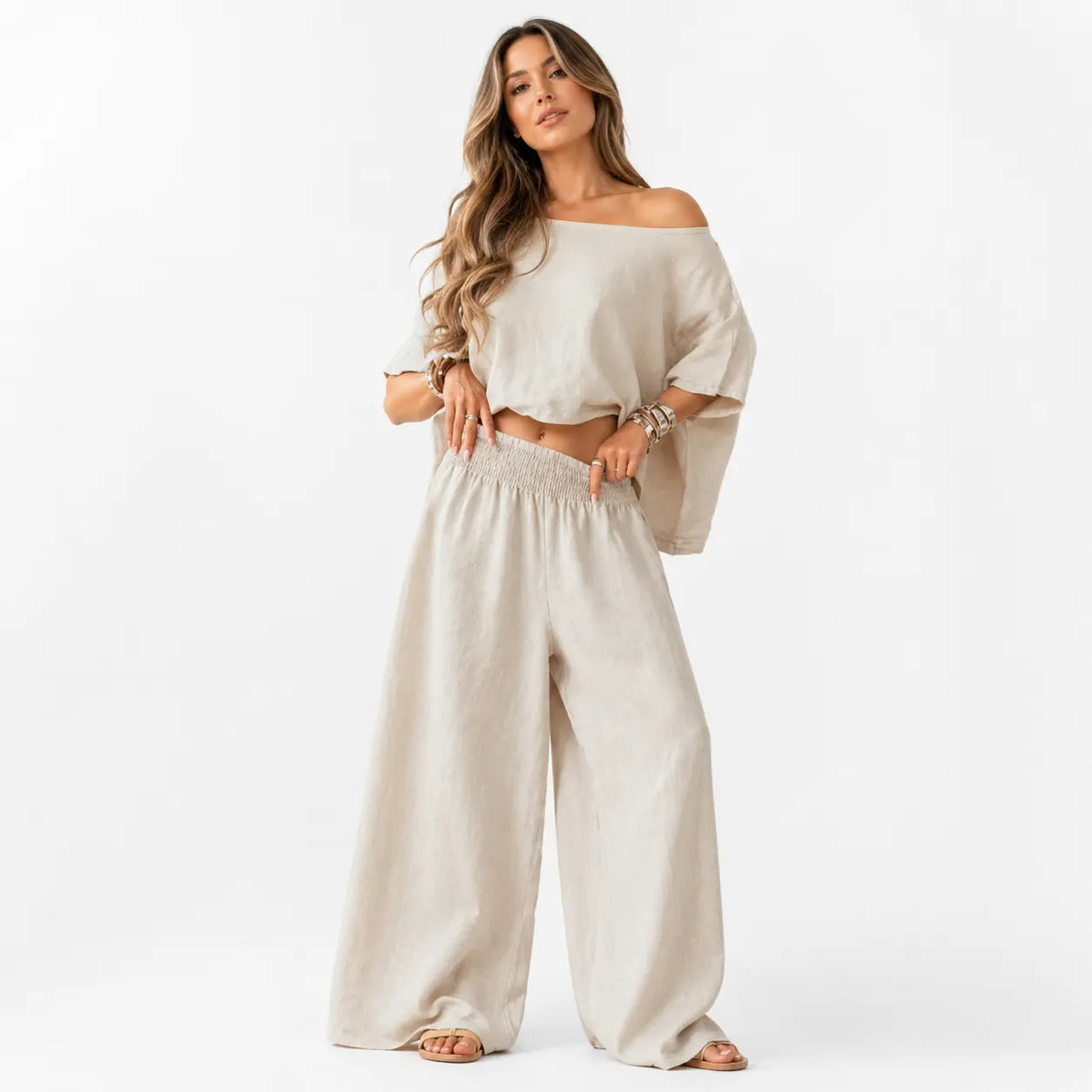 Woman wearing a beige off-shoulder top and wide-leg pants on a white background