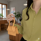 Person holding a small mustard yellow handbag in a room with plants and furniture.