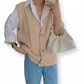 Person wearing a beige cable knit vest over a white shirt, holding a beige clutch.