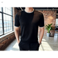 Person wearing a black mesh sweater in an indoor setting with brick walls and large windows.