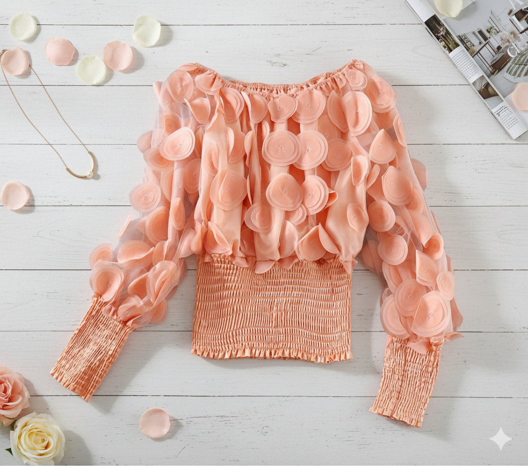 Pink blouse with ruffled sleeves on a light wooden surface with flowers and a magazine.