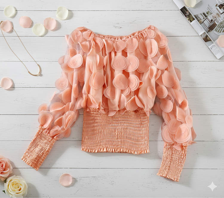 Pink blouse with ruffled sleeves on a light wooden surface with flowers and a magazine.
