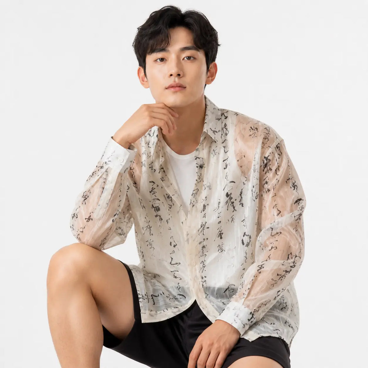 Man wearing a sheer floral shirt over a white t-shirt with black shorts on a light gray background