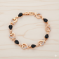 Rose gold bracelet with black gemstones on a light wood background