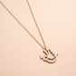 Rose gold necklace with a bird-shaped pendant on a beige background