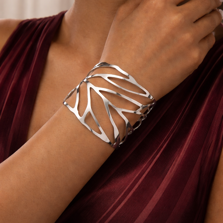 Silver leaf-patterned bracelet on a wrist with a maroon fabric background