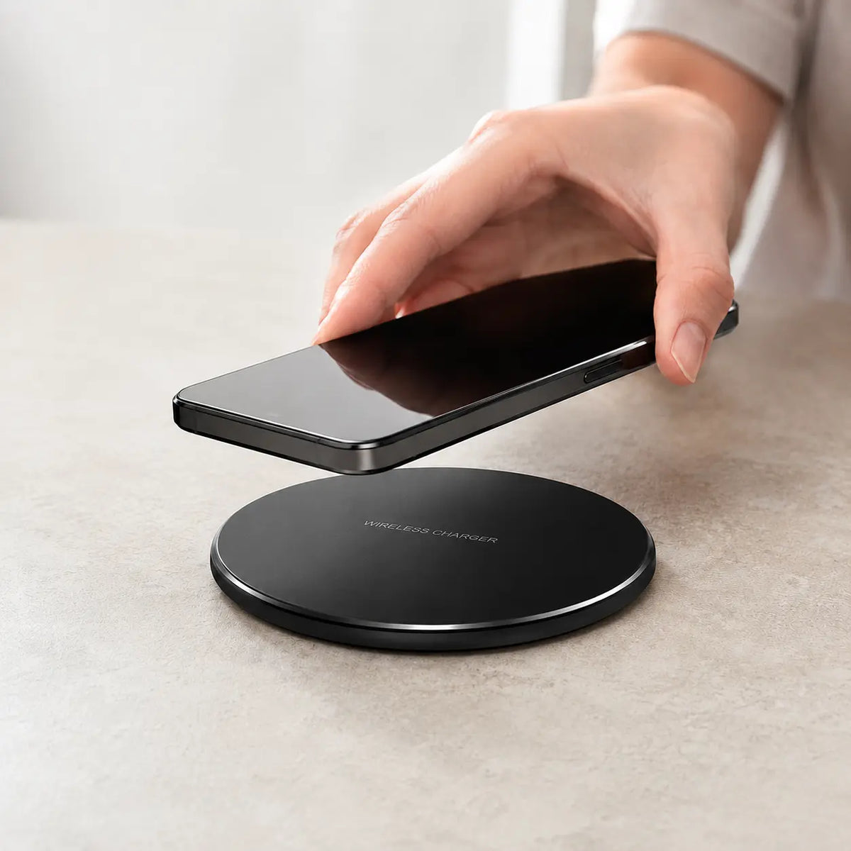 Fast wireless charger pad for iPhone and Samsung, slim black design on table with hand holding phone above